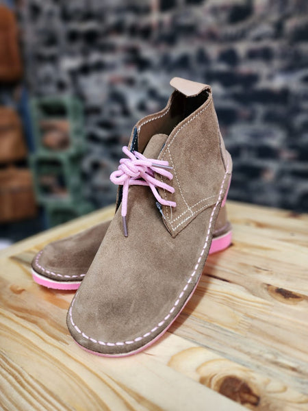 Brown boot with pink laces and soles on a wooden surface.