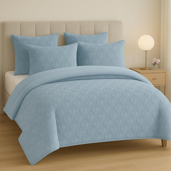 Blue quilted bedding set on a bed with matching pillows in a bedroom setting.
