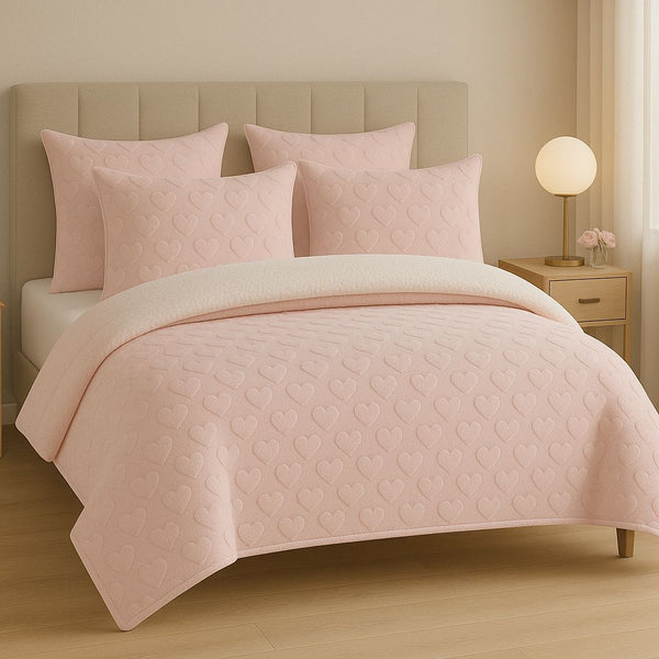 Pink quilted bedding set on a bed in a bedroom setting.